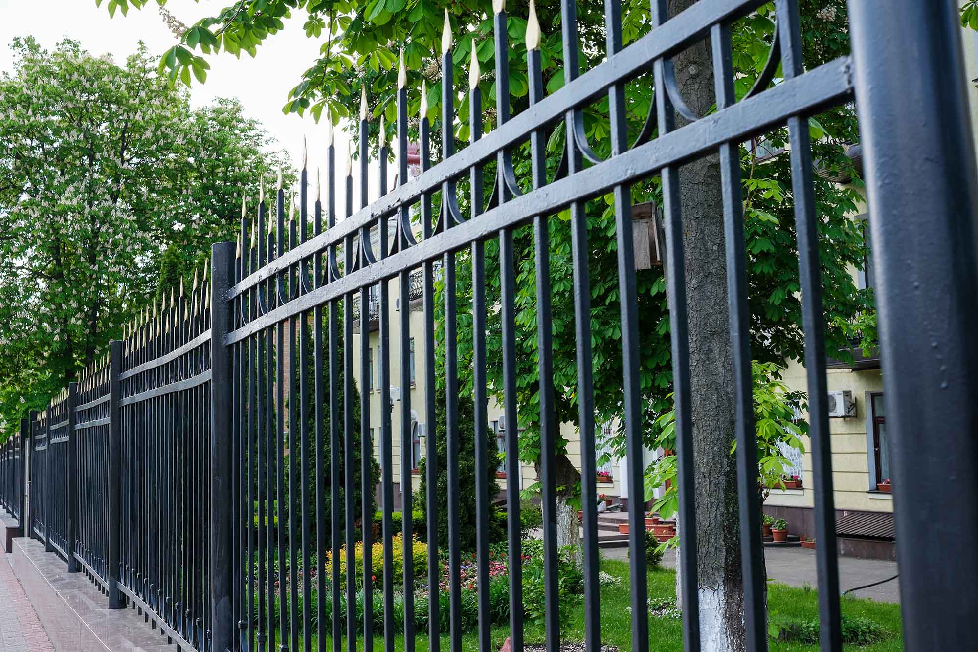 A decorative black fence encloses a vibrant garden filled with greenery.