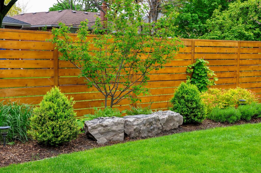 Horizontal cedar fence with a small tree and garden running the fence line.