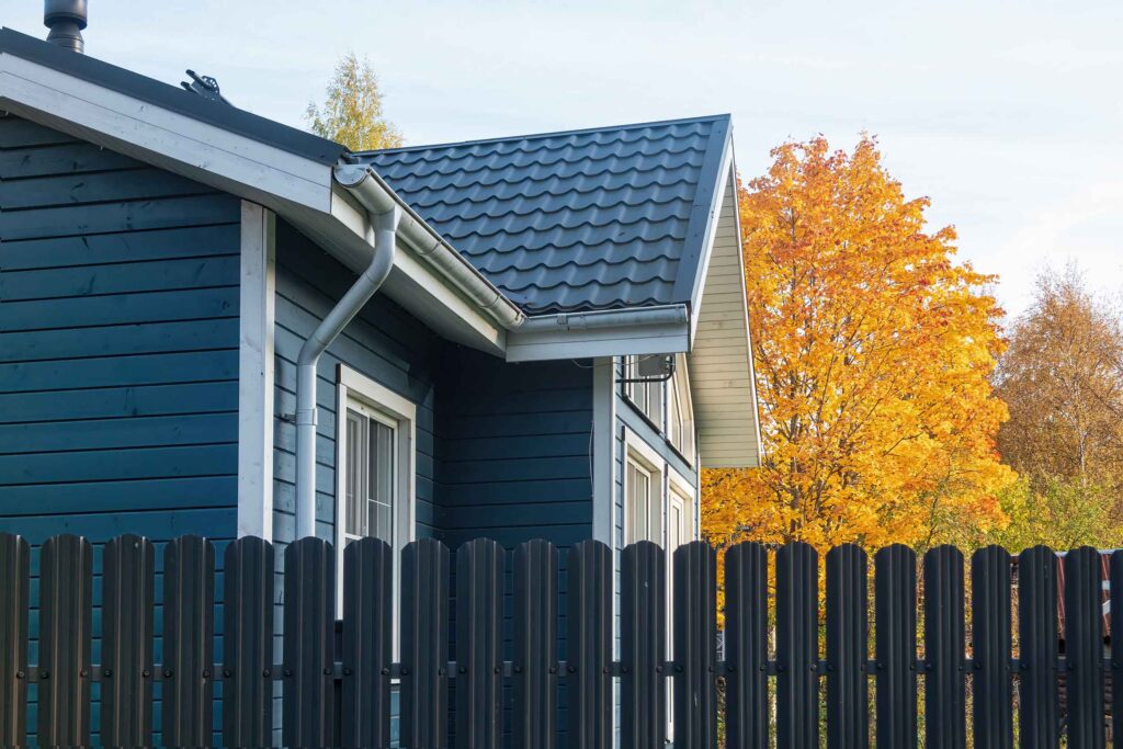 A fragment of a one-story wooden residential building behind a metal fence.